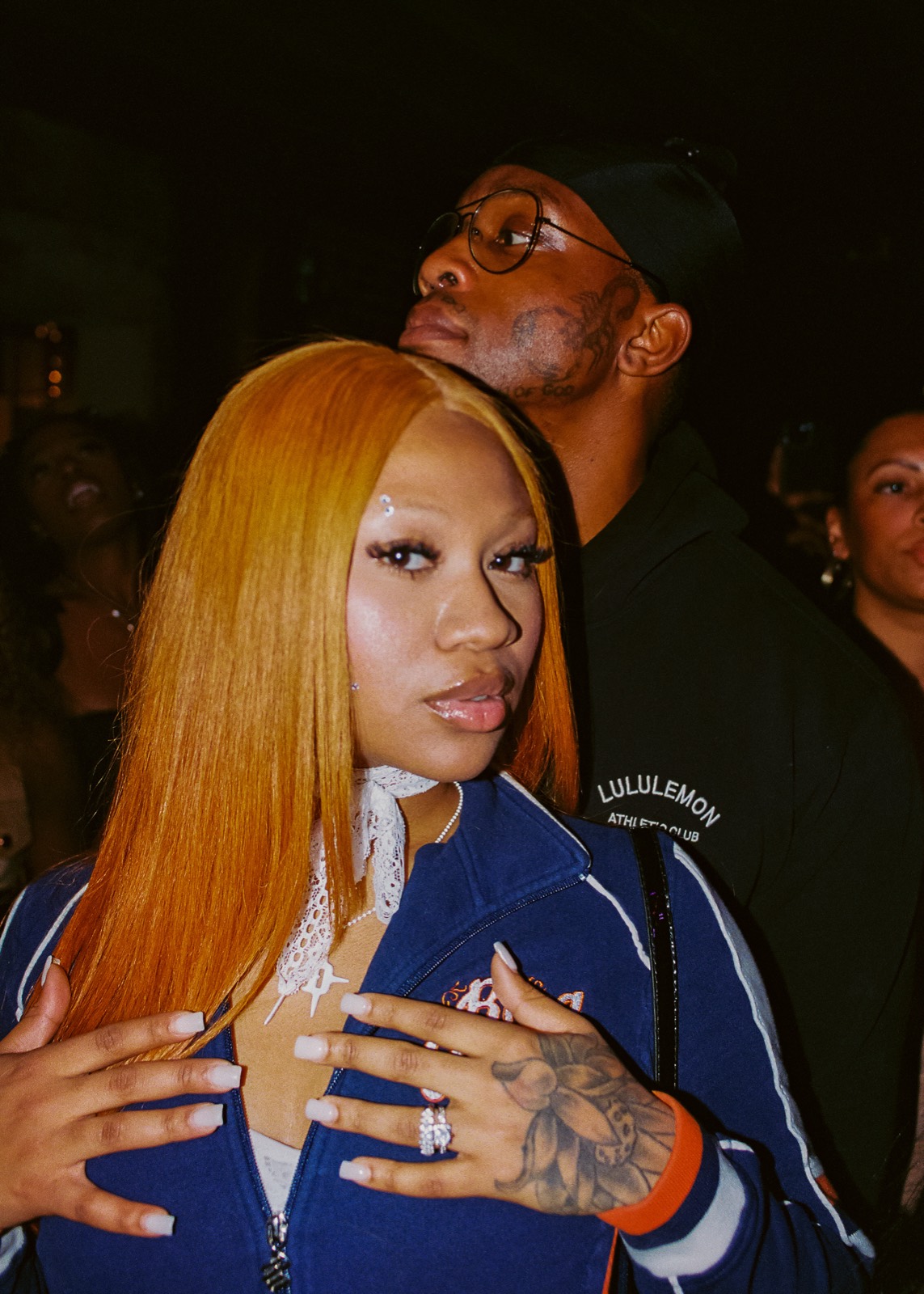 A girl with long copper hair photographed mid-event, a friend behind her
